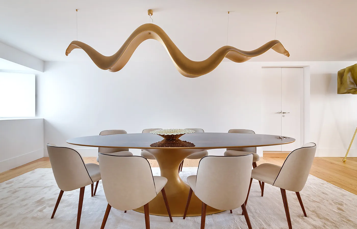 Ambiente de sala de jantar com candeeiro Aura em dourado com uma mesa de jantar Jade oval e cadeiras Europa