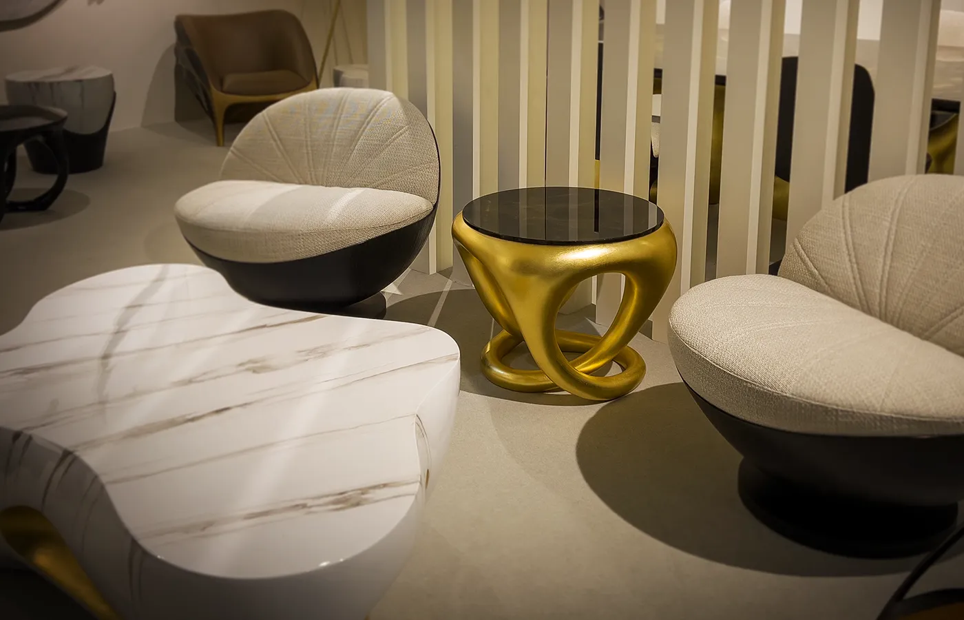 Ambiente de exposição com mesa de apoio Ballad em folha de ouro junto a cadeirões Bola e mesa de centro Oasis