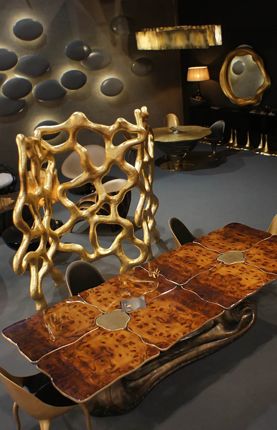 Exhibition setting with Sigma dining table in brass color and walnut root top with several Karpa pieces